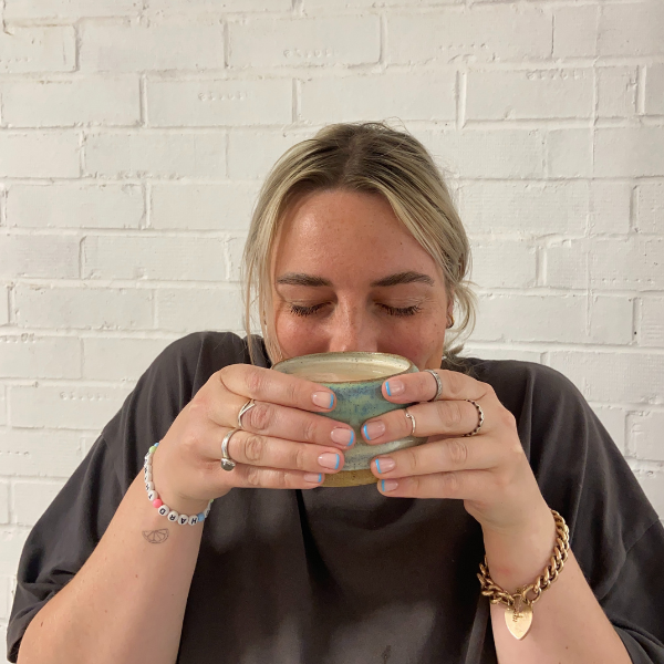 Charlie holding a small ceramic cup against a white brick wall