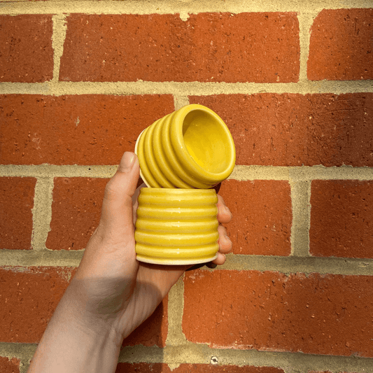 Hand holding two yellow ceramic espresso cups against a brick wall