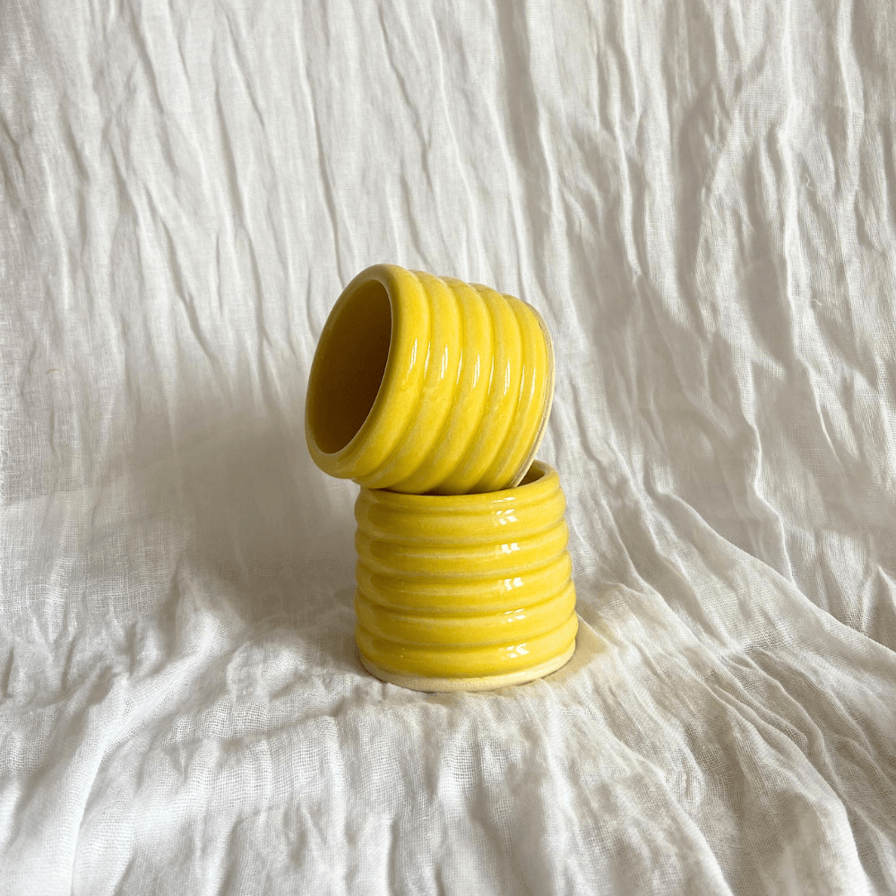 Two yellow ceramic espresso cups stacked on a white textured surface